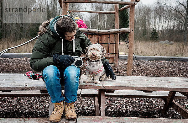 Mann saß mit seinem Hund auf einer Parkbank draußen