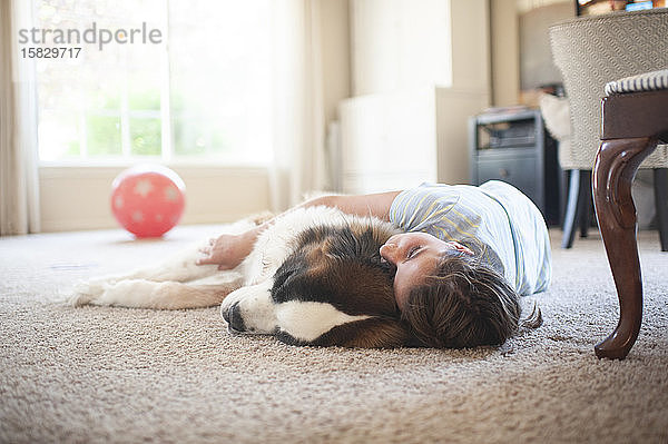 Junges Mädchen liegt mit großem Bernhardinerhund zu Hause auf dem Teppich