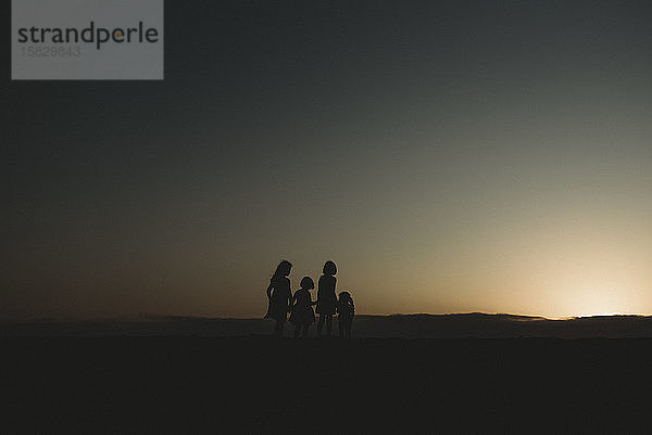 Silhouette von vier jungen Schwestern am Strand bei Sonnenuntergang