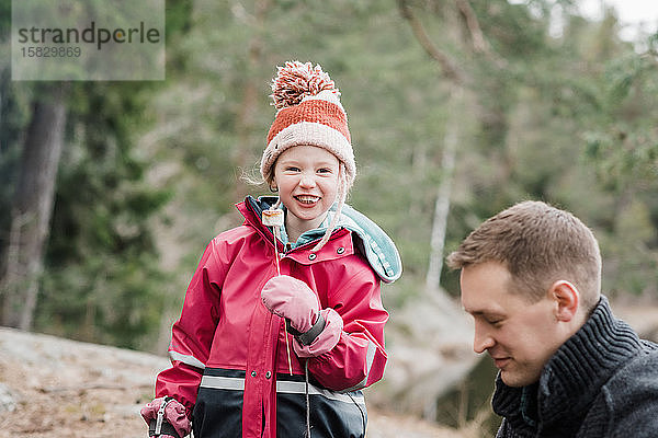 junges Mädchen lächelt und isst einen Marshmallow beim Camping in Schweden