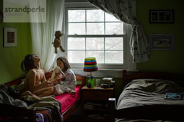 Zwei Kinder im Schlafanzug spielen mit Stofftieren in einem Schlafzimmer