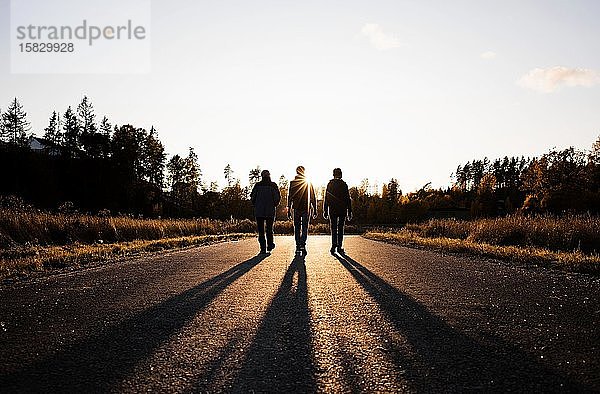 Silhouette einer Familie  die bei Sonnenuntergang eine Landstraße entlang läuft