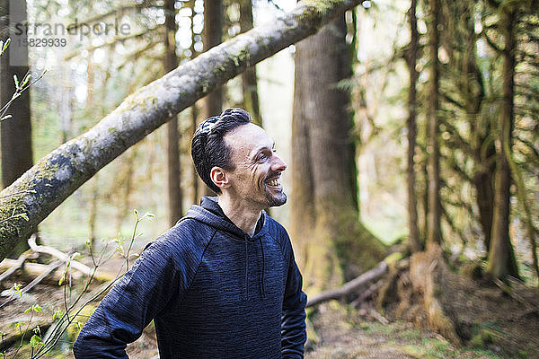 Porträt eines Mannes mit Pullover  der im Wald lächelt.