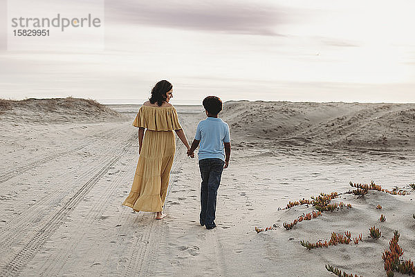 Junge Mutter und schulpflichtiger Sohn spazieren am Strand vor bewölktem Himmel