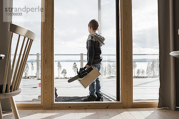 Junge spielt mit Spielzeugwerkzeugen in seinem Haus mit Blick auf das Meer