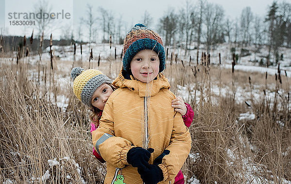 Geschwister spielen  während sie draußen im Schnee in die Kamera schauen