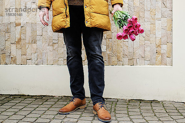 blonder Mann in einer gelben Winterjacke mit einem Tulpenstrauss in den Händen
