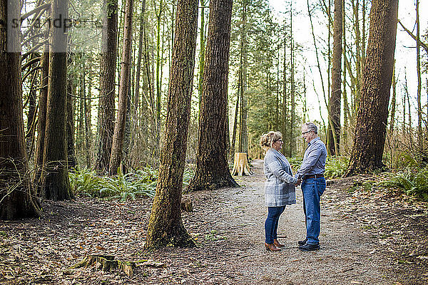 Älteres Paar  das sich im Wald an den Händen hält und einander anschaut.