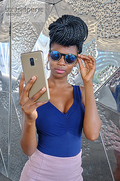 junge schwarze Frau mit sehr langen Zöpfen und sehr attraktiv und sinnlich genießt barcelona im Sommer und macht Model mit Handy  Brille und Kamera  Technikkonzept.