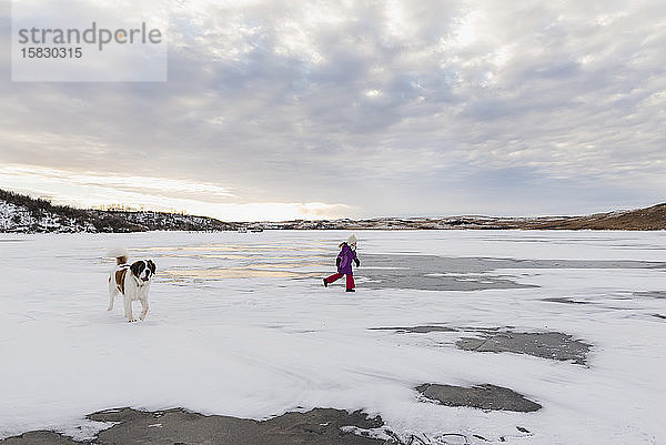 Kleines Mädchen rennt mit Hund auf gefrorenem See