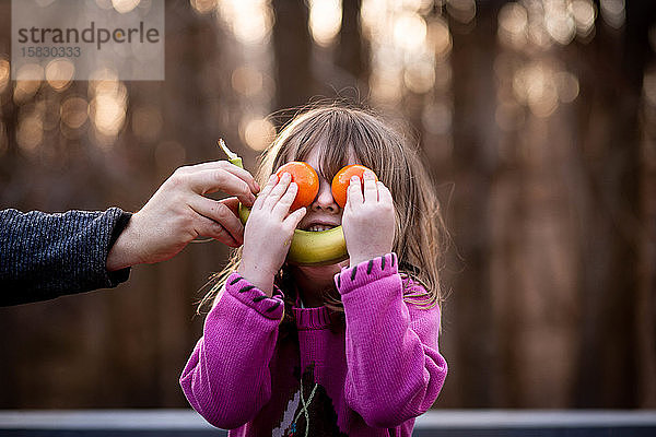 Junges Mädchen legt Obst auf das Gesicht  um draußen ein albernes Gesicht zu machen