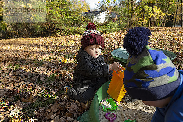 Zwei von Blättern umgebene Brüder spielen in der Herbstsaison im Sandkasten