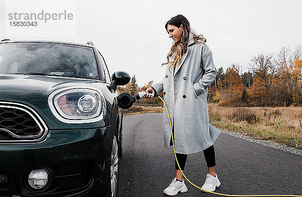 Frau  die ihr Elektroauto auf einer Landstraße in Schweden einsteckt