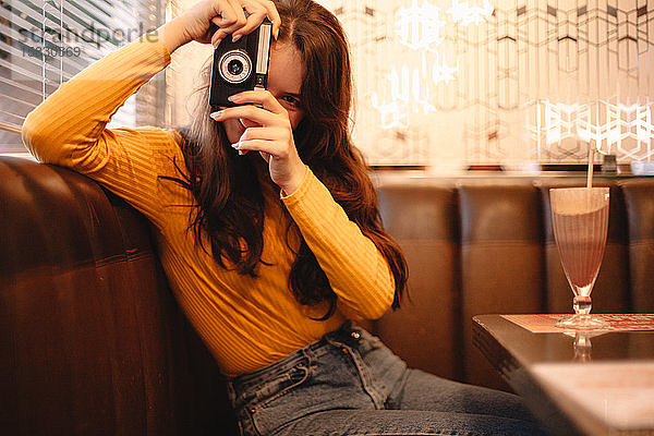 Glückliches Teenager-Mädchen fotografiert mit Vintage-Kamera im Café