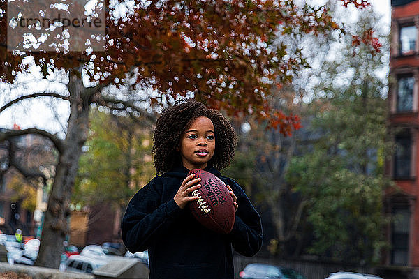 Mädchen schaut weg  während sie American Football in der Stadt hält