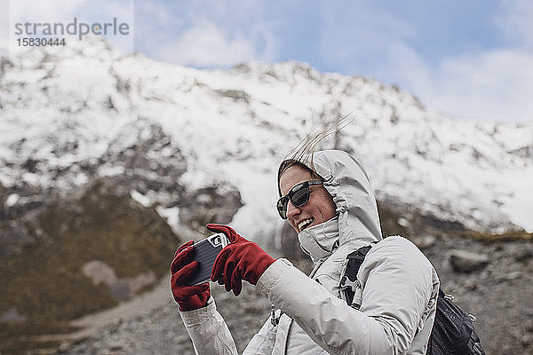 Wanderin mit benutzter Handykamera an windigem Tag in den Bergen.