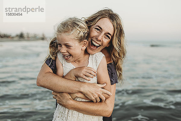 Mutter umarmt junges Mädchen mit Sommersprossen im Meer lachend