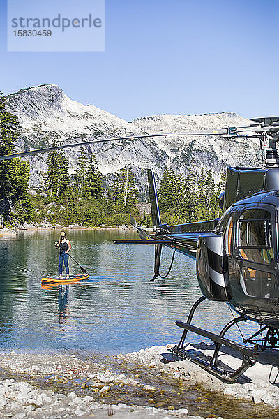 Aktive Frau paddelt auf einem abgelegenen See  zu dem ein Hubschrauber Zugang hat.
