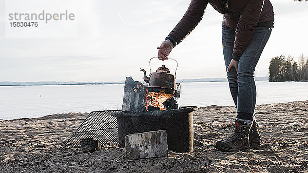 Frau  die einen Wasserkessel über ein Lagerfeuer am Strand in Schweden hält