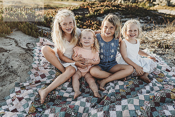 Vier Schwestern sitzen am Strand auf einer Decke und lächeln bei Sonnenuntergang