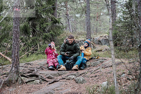 Papa sitzt im Winter beim Wandern mit seinen Kindern und macht ein Picknick