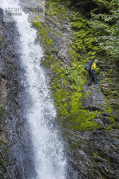 Mann blickt beim Abseilen neben einem Wasserfall nach unten  B.C. Kanada