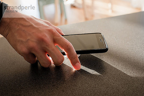 Mann hält zu Hause in der Küche ein Telefon in der Hand