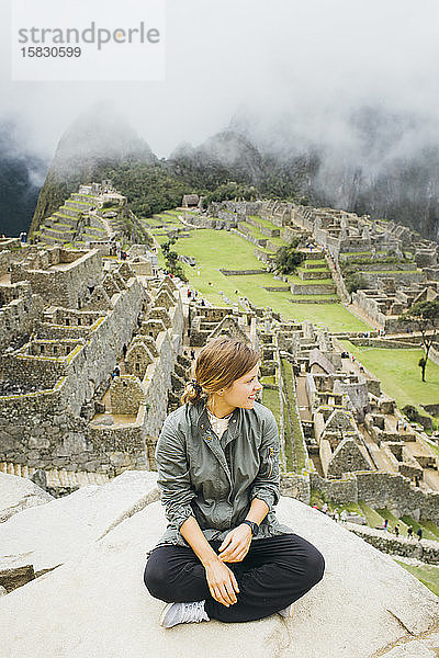 Eine junge Frau sitzt in der Nähe der Ruinen von Machu Picchu  Peru