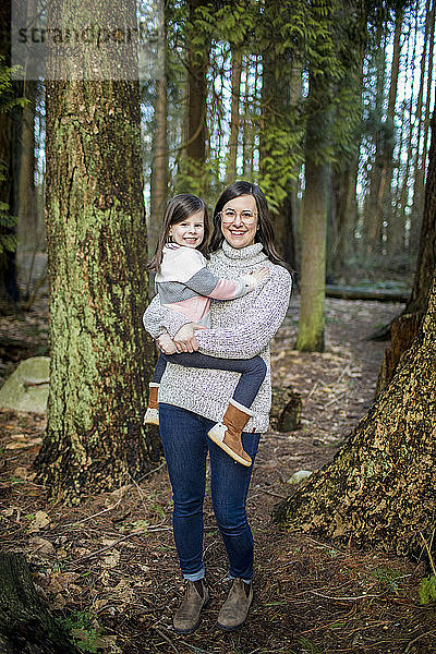 Mutter hält ihr süßes kleines Mädchen im Wald.