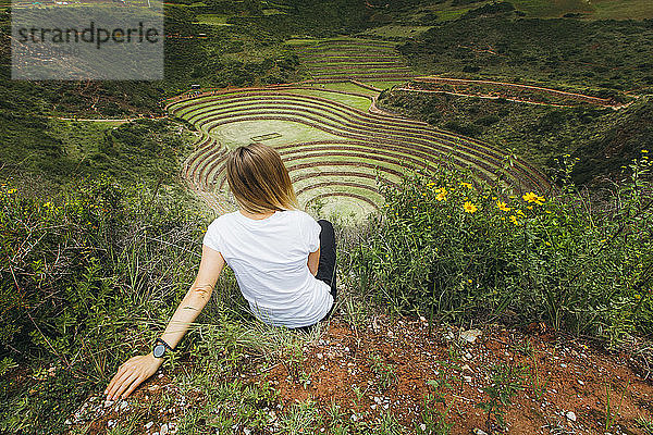 Eine junge Frau sitzt in der Nähe des berühmten peruanischen Fleckens Moray in Peru