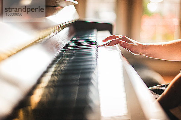 Ausgeschnittenes Bild einer Kinderhand  die in einem sonnigen Raum Klavier spielt.