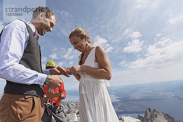 Braut steckt dem Bräutigam während der Hochzeit auf dem Berggipfel einen Ring an den Finger  Wyoming
