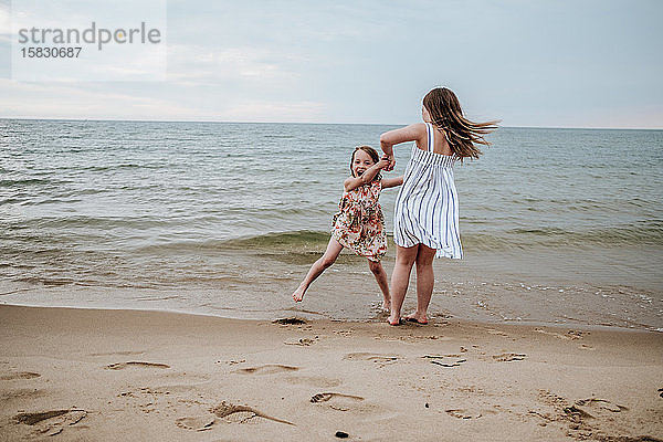 Schwestern tanzen und spielen am Strand des Lake Michigan
