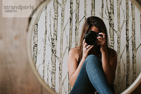 Frau mit Kamera in der Hand  die ihr Spiegelbild im Spiegel fotografiert.