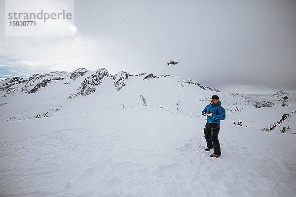 Mensch fliegt Drohne in Winterlandschaft.