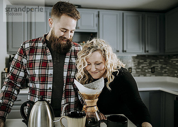 junge Frau riecht Morgenkaffee  während Ehemann mit Bart zuschaut