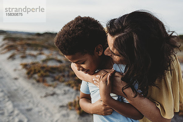 Seitenansicht Nahaufnahme-Porträt einer jungen Mutter  die ihren Sohn am Strand umarmt