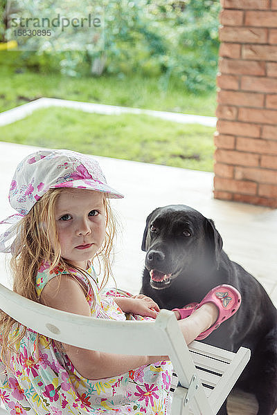 Mädchen sitzt mit einem großen schwarzen Hund auf dem Hof