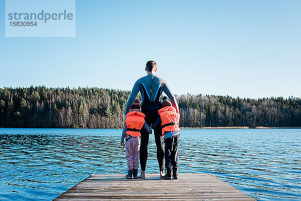 Vater und seine Kinder stehen am Ende eines Piers und schauen aufs Meer