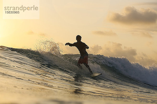 Junger Mann surft bei Sonnenuntergang