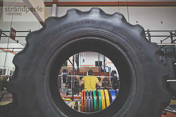 Blick durch den Reifen eines Bodybuilders  der in der Turnhalle Kniebeugen macht
