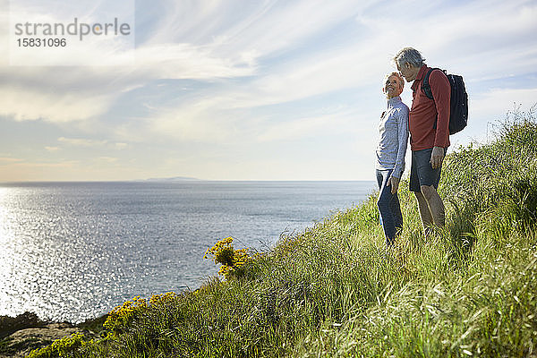 Älteres Ehepaar spricht  während es auf einer Klippe am Meer gegen den Himmel steht