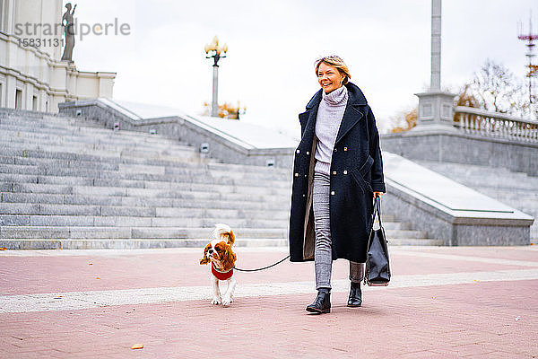 Eine Frau spaziert mit einem Cavalier King Charles Spaniel Hund durch die Stadt.