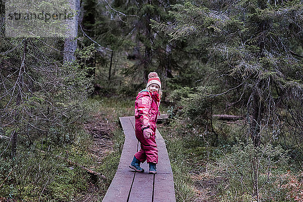 Lächelndes Mädchen  das im Winter über eine Strandpromenade im Wald läuft