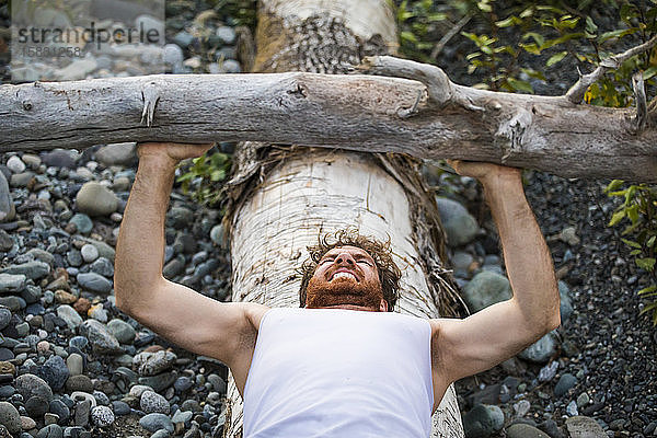 Mann drückt während eines Trainings im Freien einen umgefallenen Baum.
