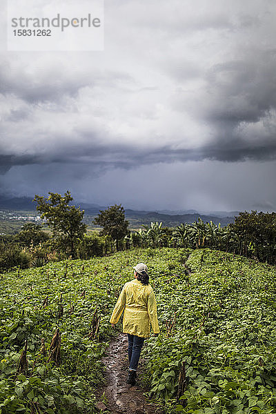 Junge Frau in gelbem Mantel geht durch üppiges Feld in Guatemala.