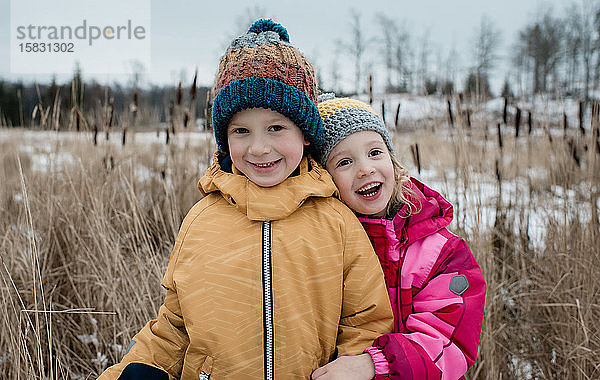 Geschwister schmusen und lachen  während sie im Winter draußen spielen