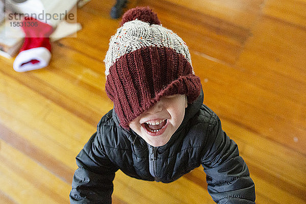 Lächelndes Kleinkind Junge mit Winterhut lacht mit von Hut bedecktem Redakteur