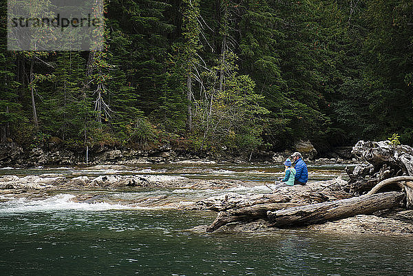 Mann und Kind sitzen in einem Fluss im Staat Washington beim Holzfischen