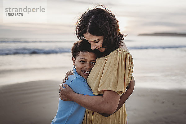Porträt einer schönen Mutter  die ihren kleinen Sohn bei Sonnenuntergang am Strand umarmt